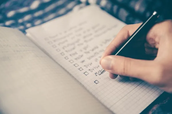 Mano escribiendo una lista de tareas en una libreta