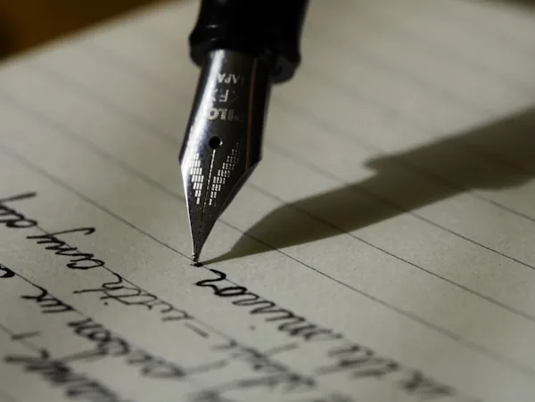 Mano escribiendo con pluma sobre papel